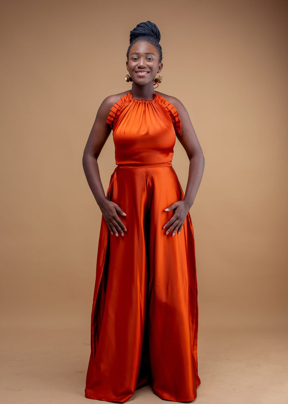 Woman in orange satin halter-neck flare pants set standing against beige background