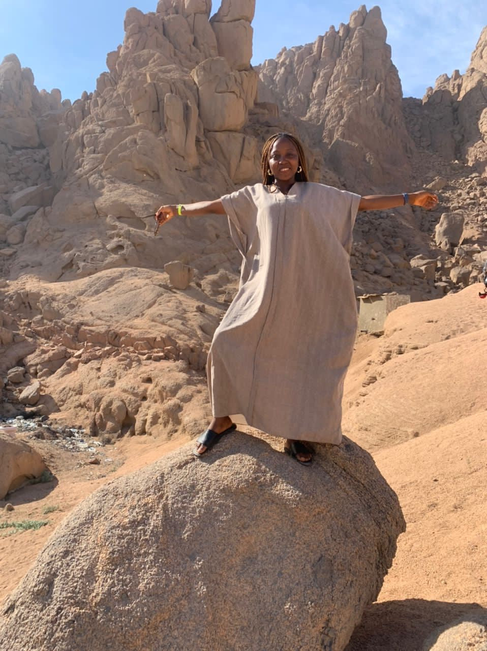 Woman in a loose beige kaftan standing on a rock in a rocky desert landscape