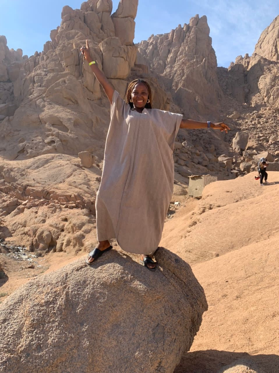 Smiling woman in flowing kaftan standing on rock with desert mountains in the background