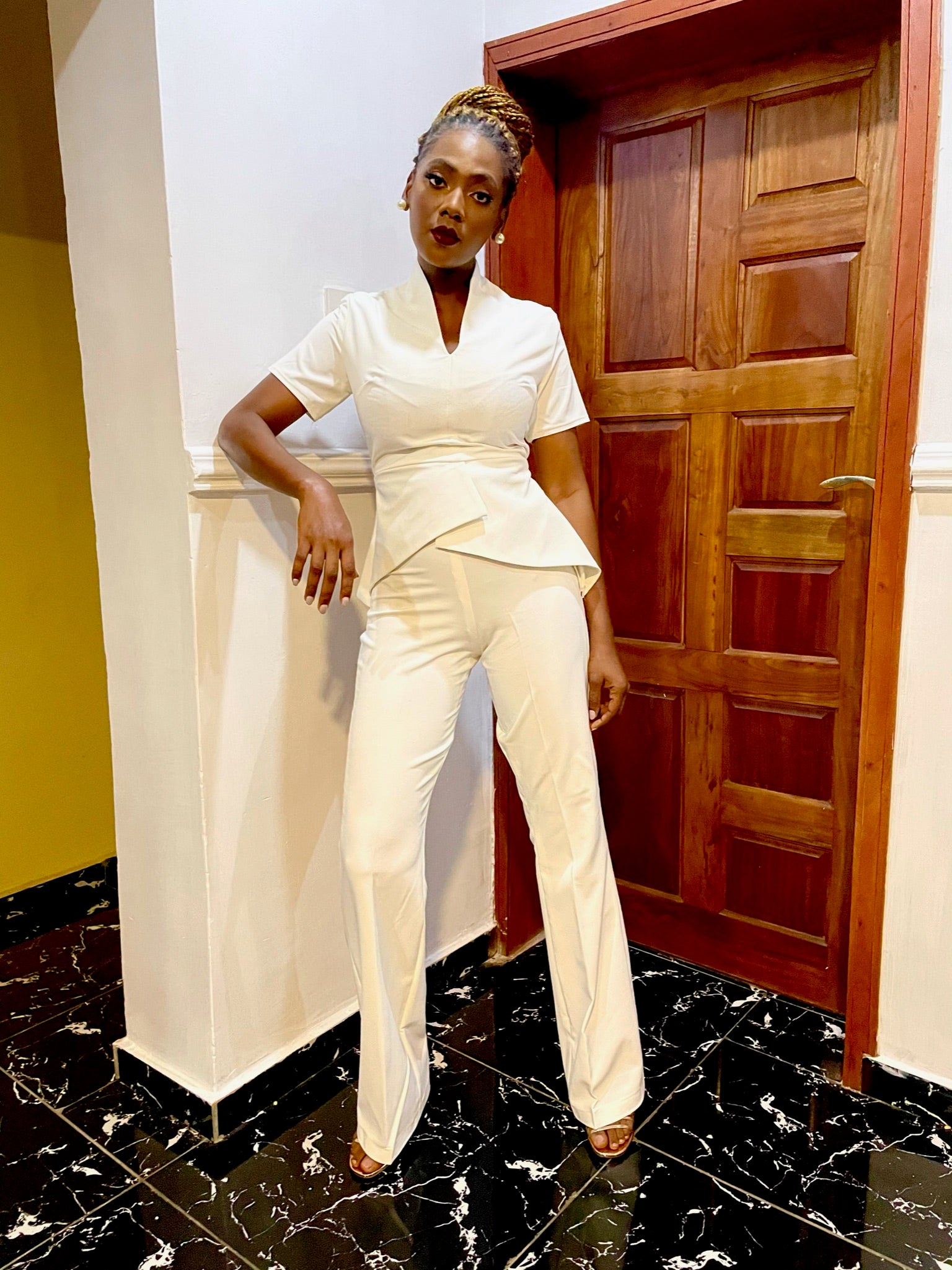 Woman wearing stylish white tailored pantsuit, posing indoors with braided hair