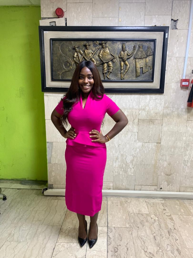 Woman in pink fitted dress posing indoors, standing on marble floor, with wall art behind her