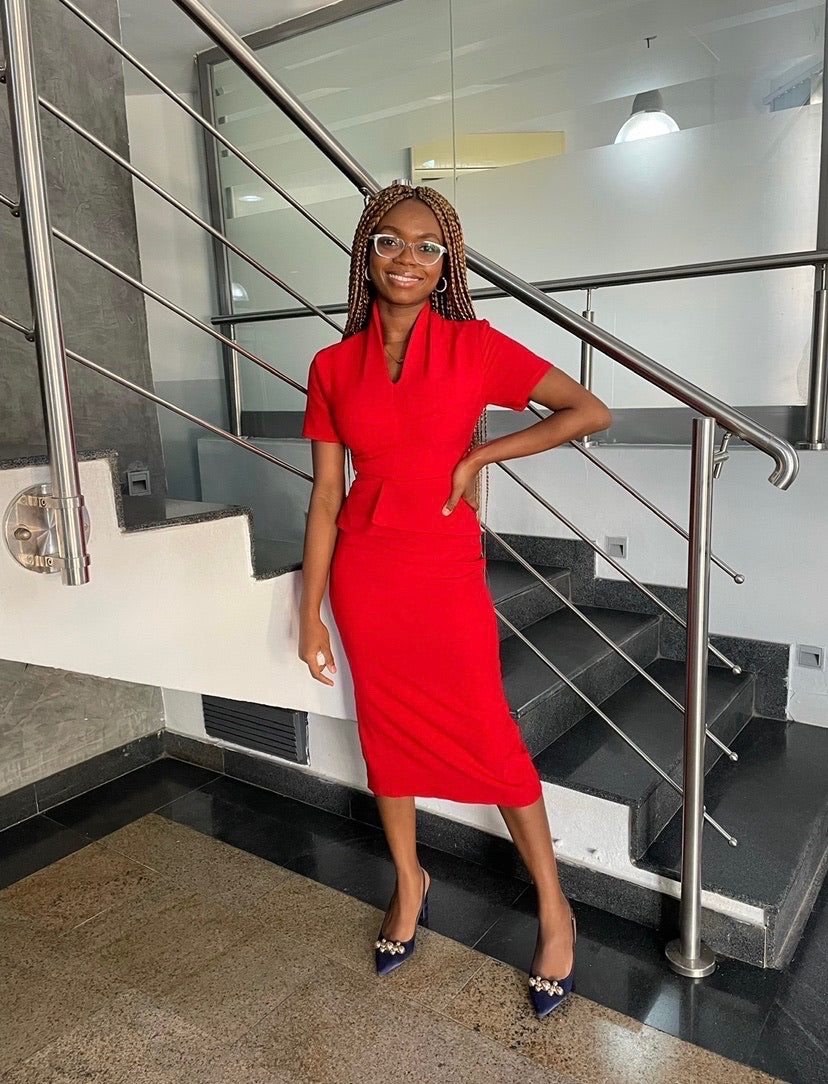 Smiling woman in a fitted red dress and heels standing indoors by modern staircase