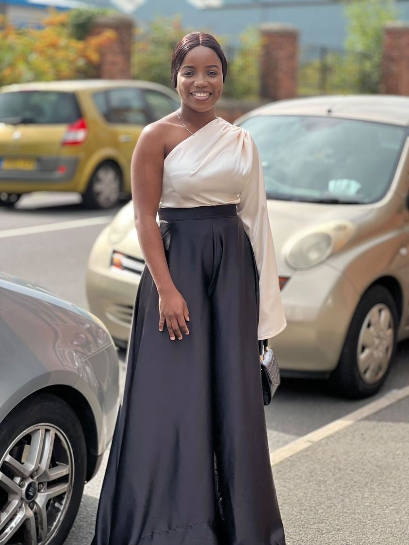 Smiling woman in elegant one-shoulder satin evening gown, standing outdoors