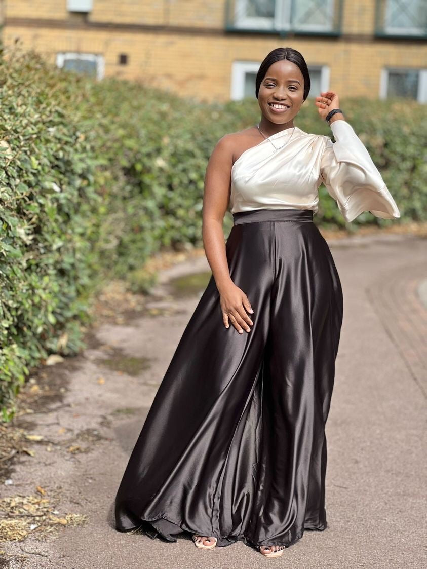 Woman in elegant satin one-shoulder jumpsuit with wide-leg pants, smiling outdoors