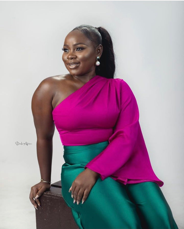 Smiling woman in magenta one-shoulder blouse and green satin skirt, studio portrait