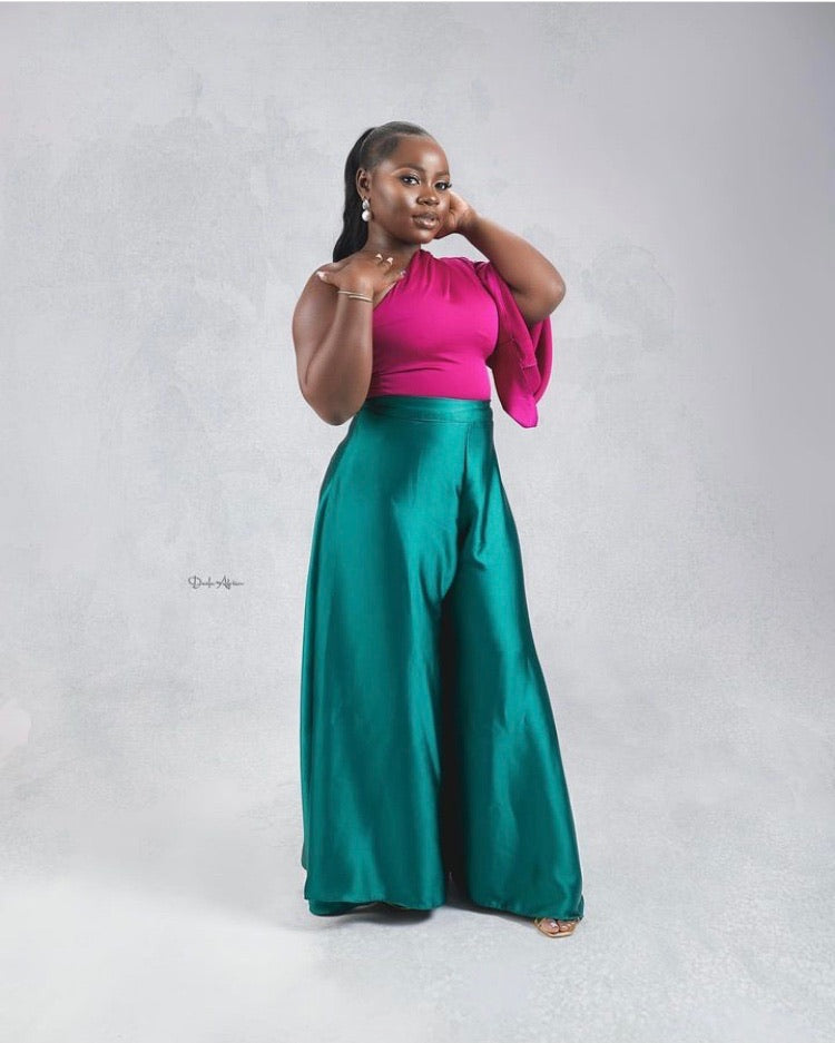 Woman in magenta one-shoulder blouse and teal wide-leg pants posing in studio