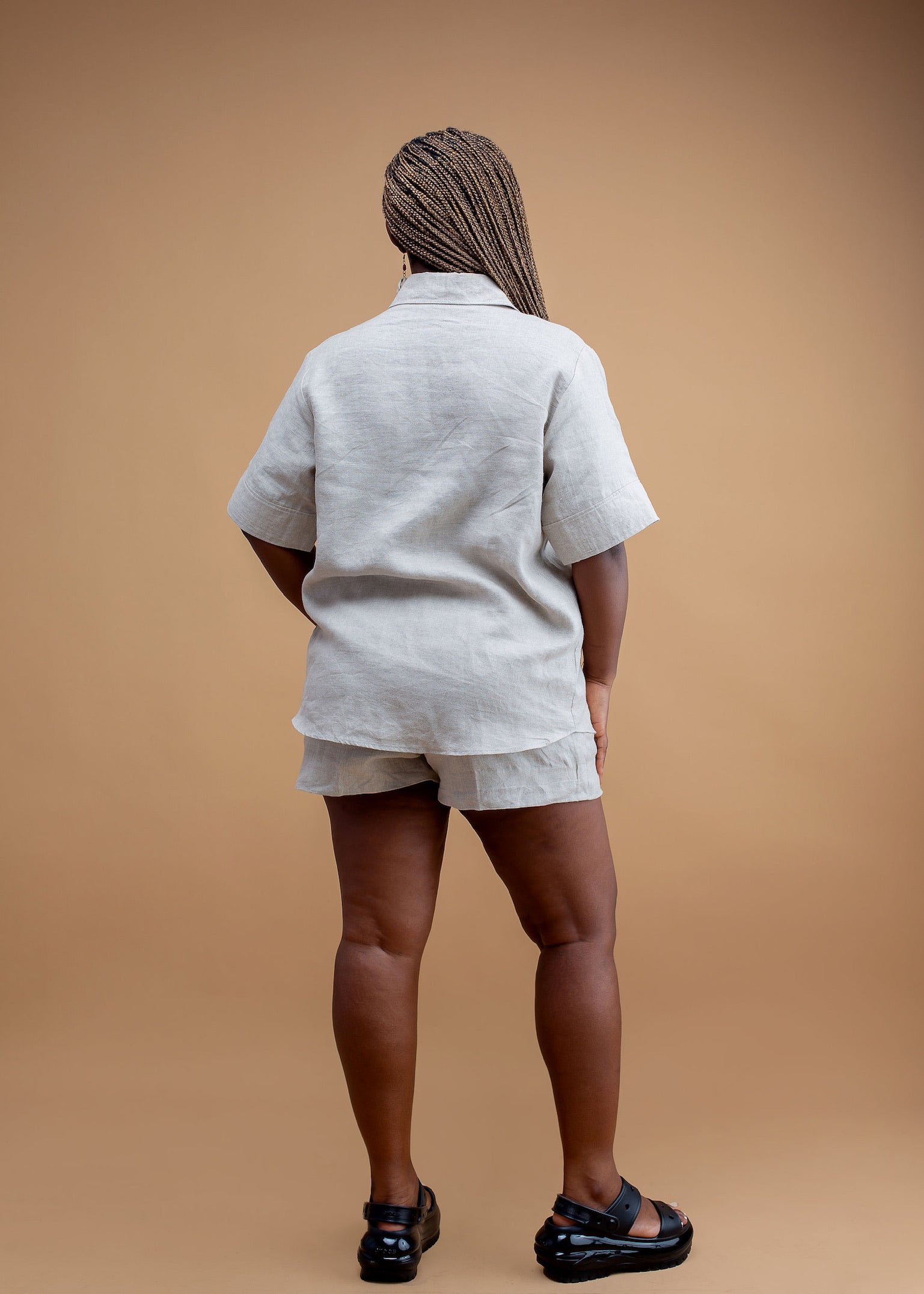 Woman in beige linen shorts and shirt set, standing against a tan background