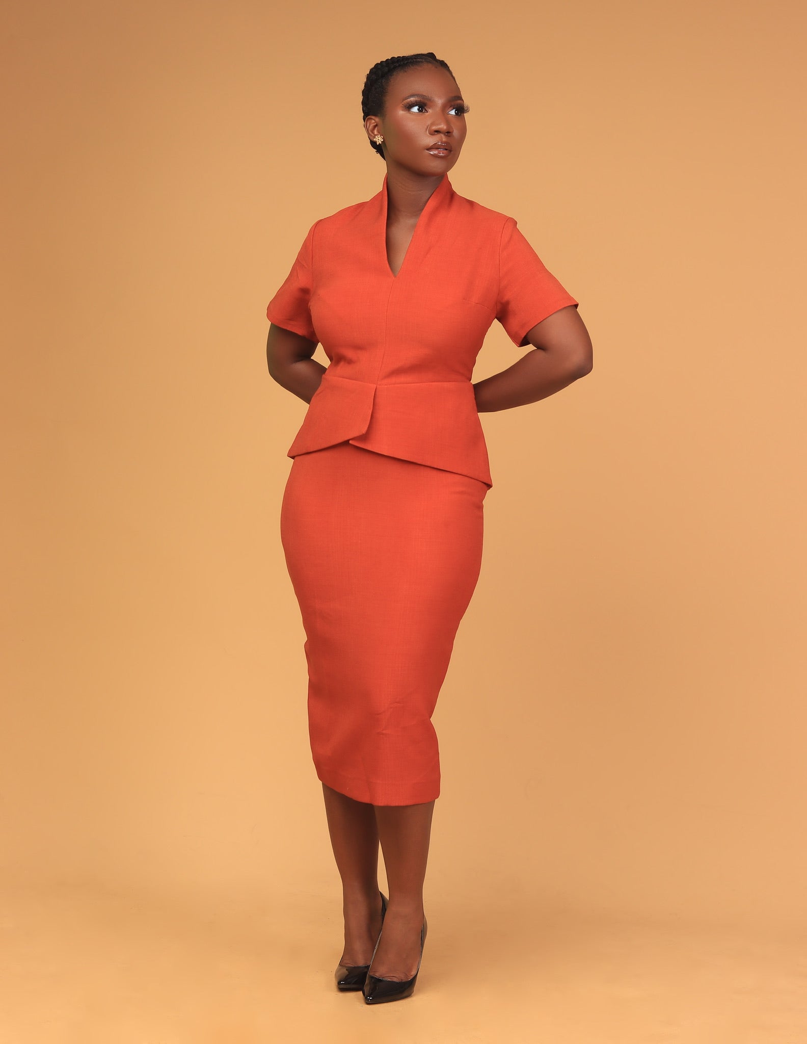 Woman wearing orange tailored skirt suit standing against neutral background