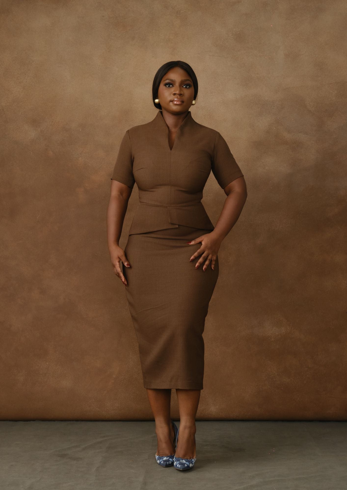 Woman in fitted brown midi dress with short sleeves standing against brown backdrop