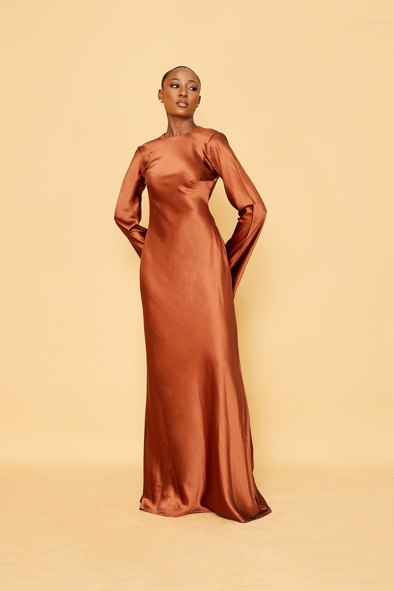 Woman in rust satin long sleeve evening gown posing against a beige background